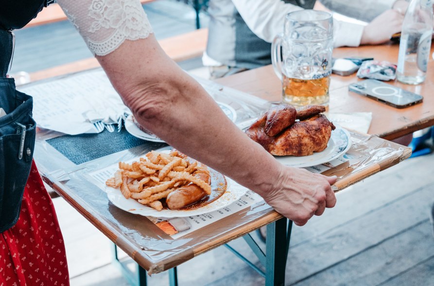 Halbes Hendl und Currywurst wird von Bedienung serviert, &copy; Inn-Salzach Tourismus